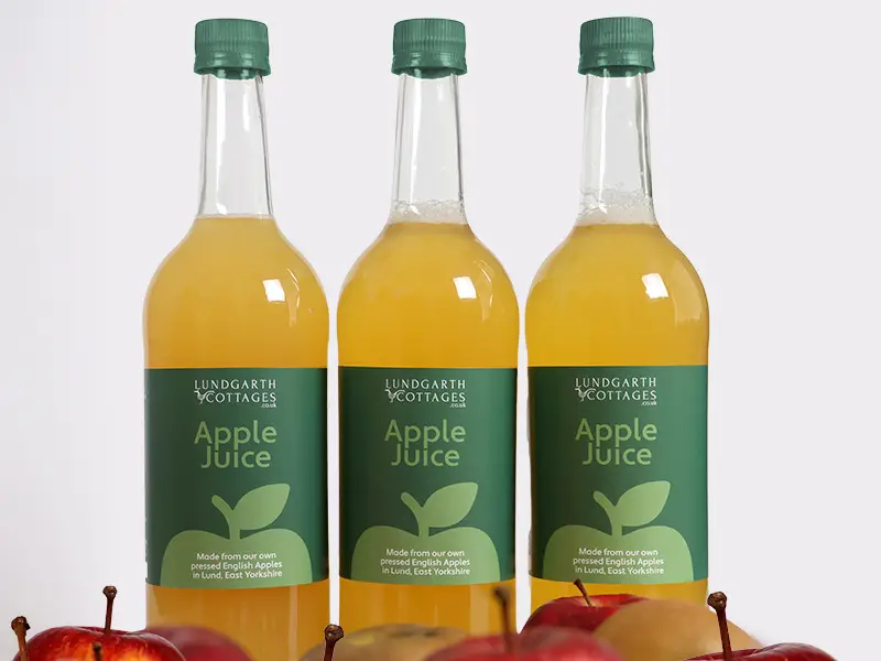 Three Lundgarth Apple Juice bottles sit behind a pile of fresh crisp apples