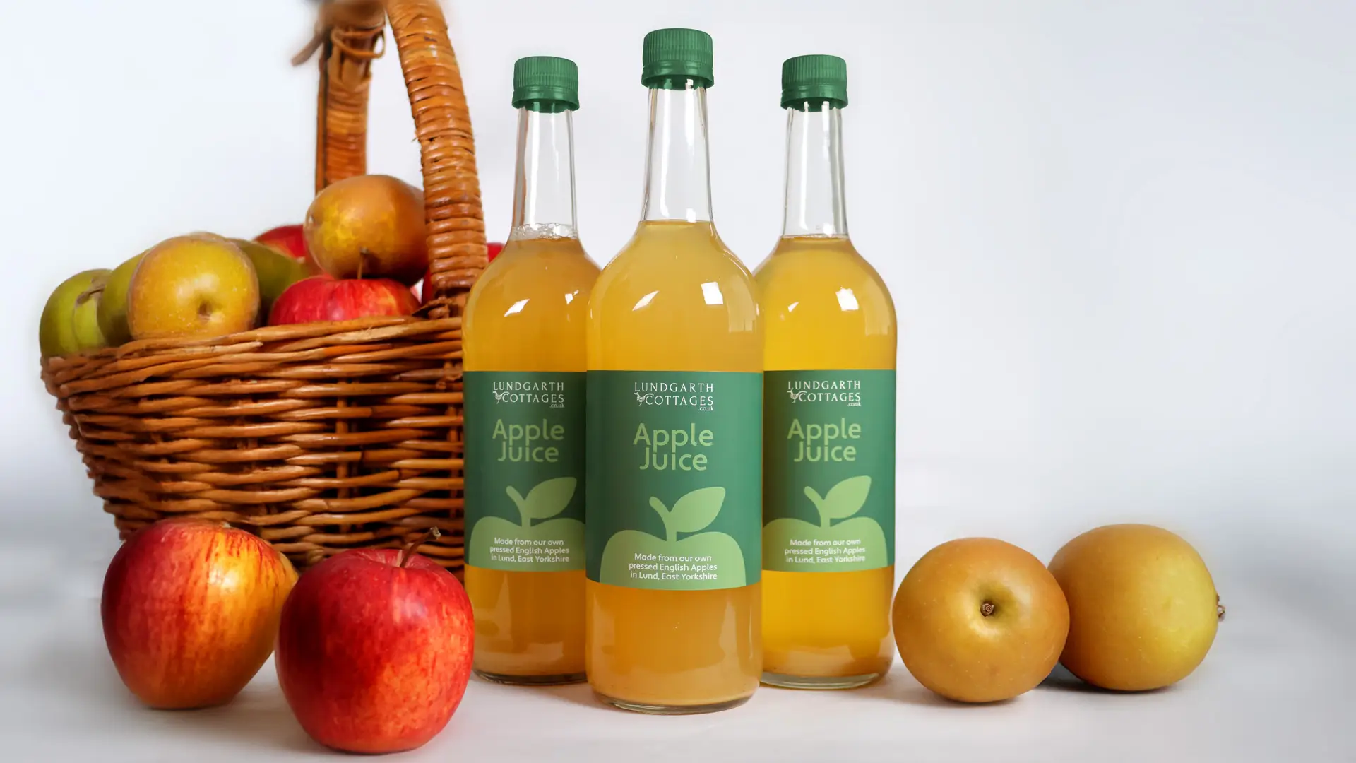 Lundgarth Apple Juice bottles featuring the new brand and packaging beside a basket of rosy red apples