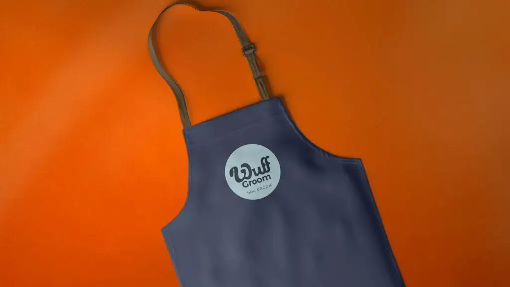 Dark blue Wuff Groom branded apron on an orange background